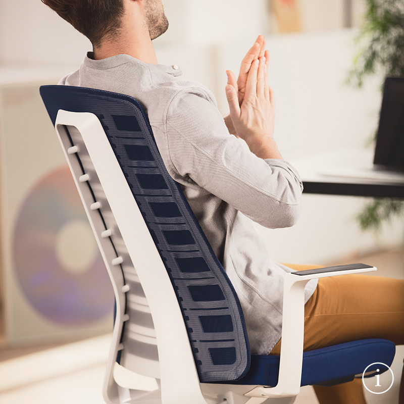 Young man, sitting on the PURE and using the unique opening in the upper backrest. The PURE ergonomic office chair is pictured from a side view with blue mesh backrest, blue seat cover, white arm pads, plastic parts and white column. Further information is available via the information button on the bottom right | by Andreas Krob & Joachim Brüske, b4k
